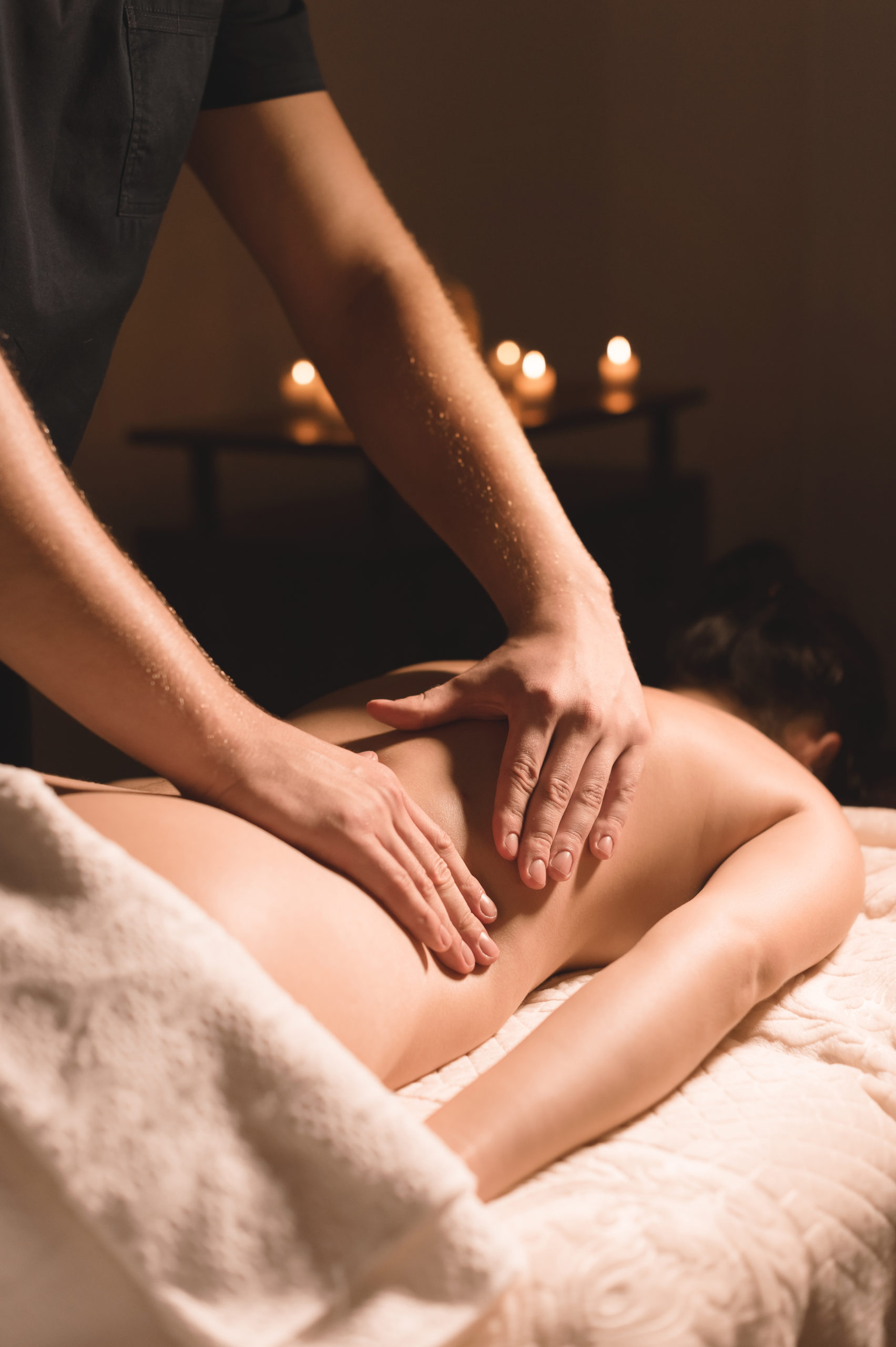 Close-up male hands doing healing massage with oil to a young girl in a dark cosmetology office. Dark key
